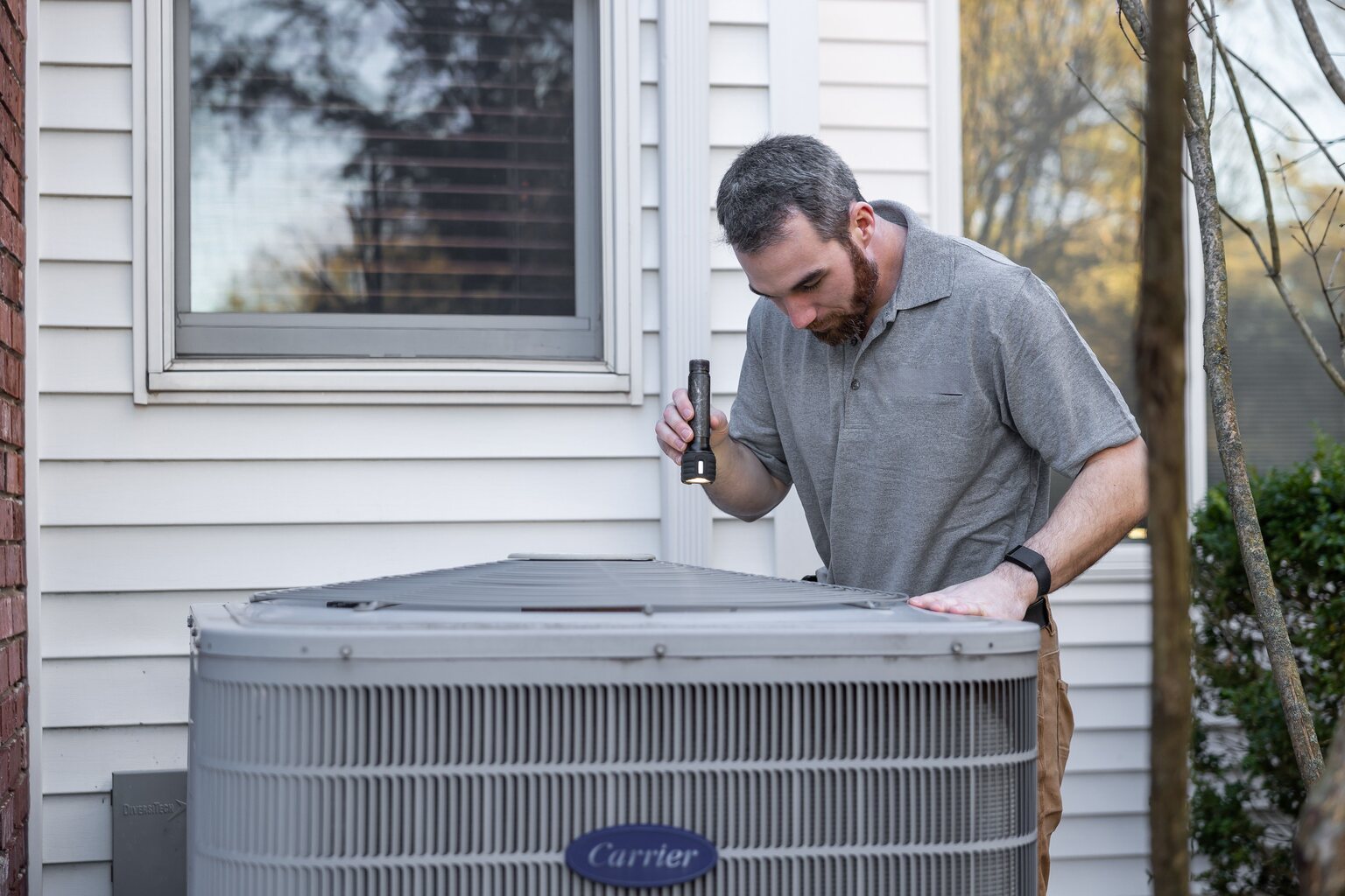 Technician inspecting a residential outdoor air conditioner during maintenance